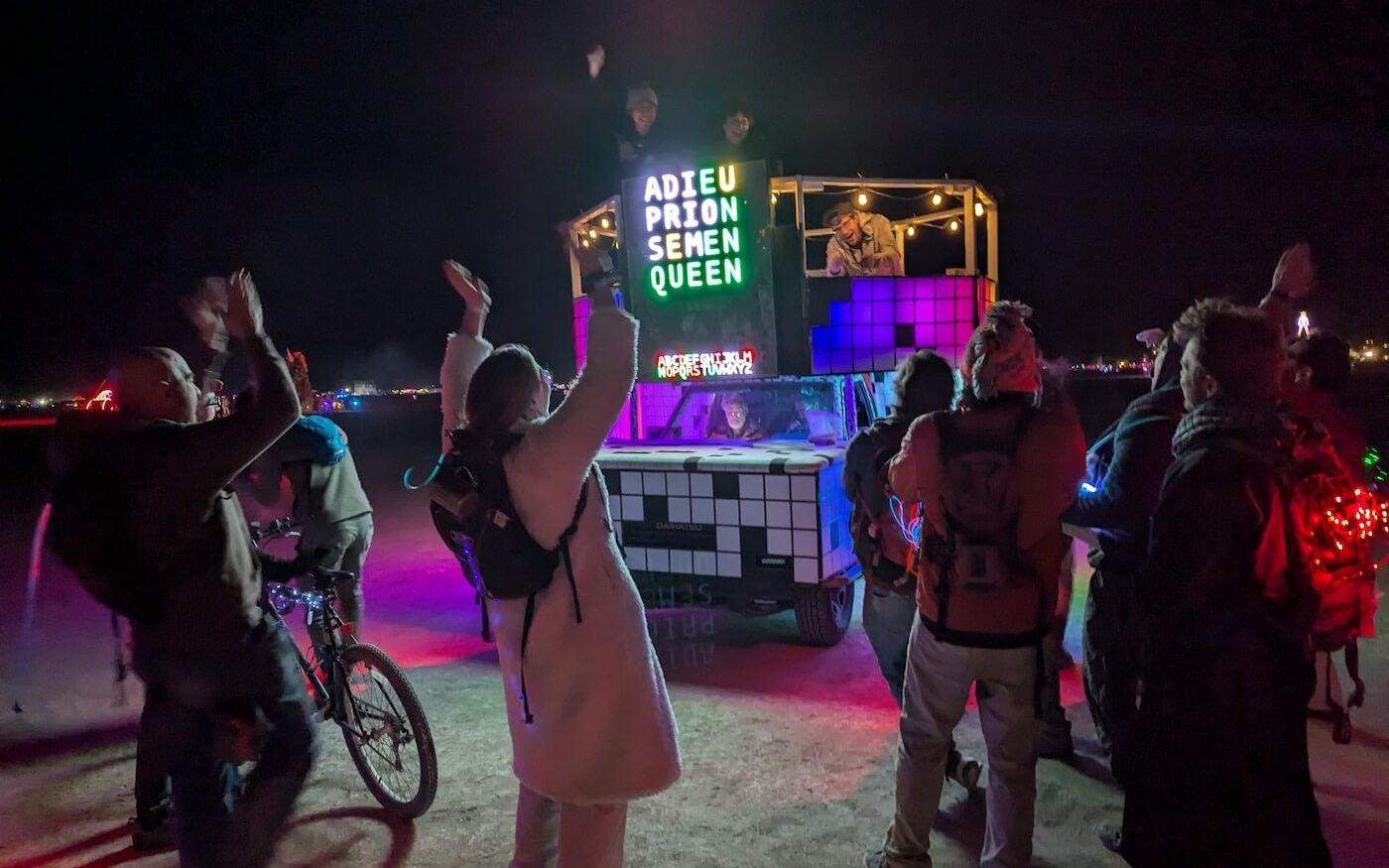 A large-format LED word-game display on a Burning Man art car showing a Wordle-style board, with a crowd gathered around at night.